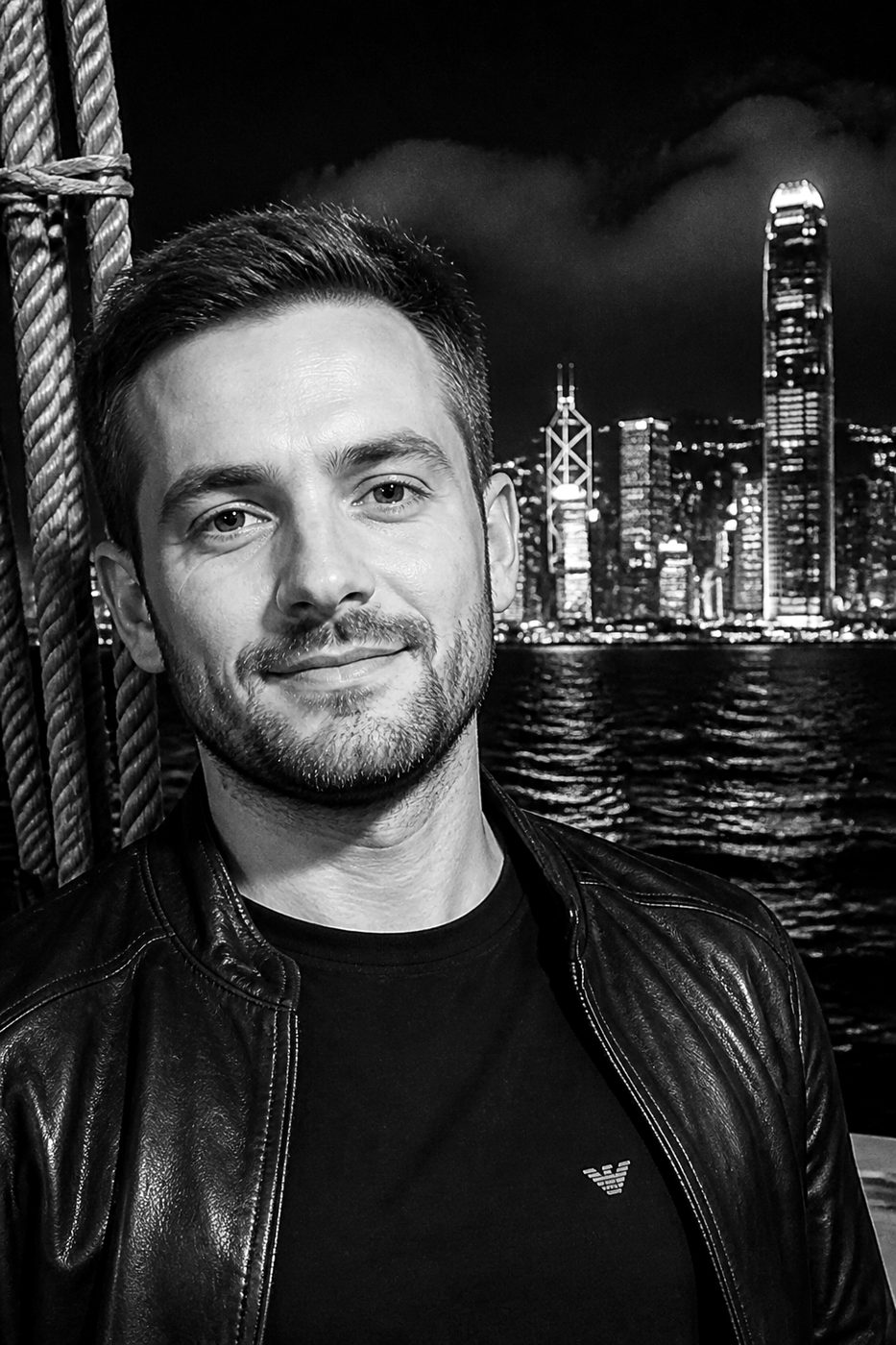 Jesse Justin, black-and-white portrait on a night boat with a city skyline behind him